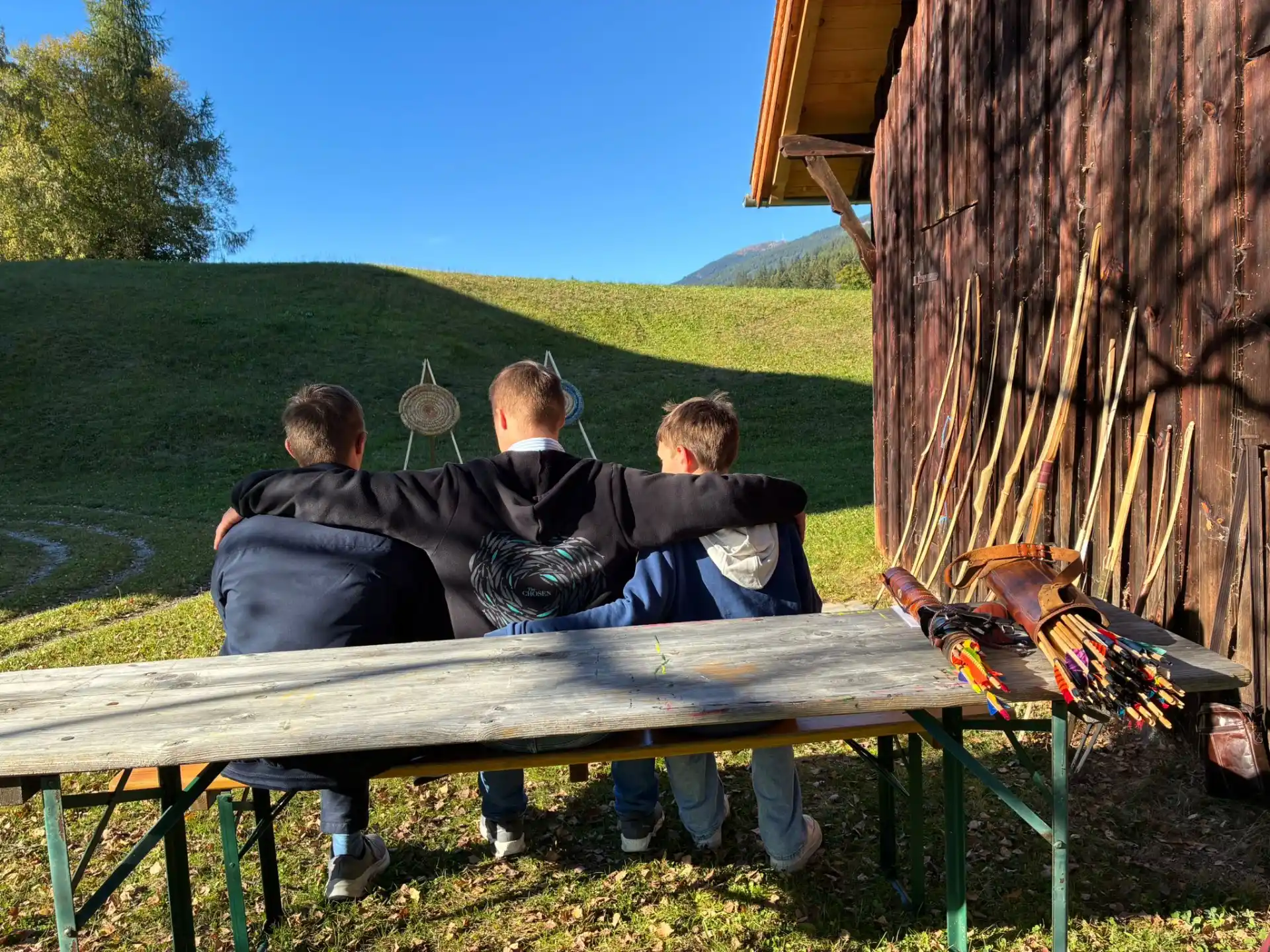 Drei Burschen mit Pfeil und Bogen umarmen sich